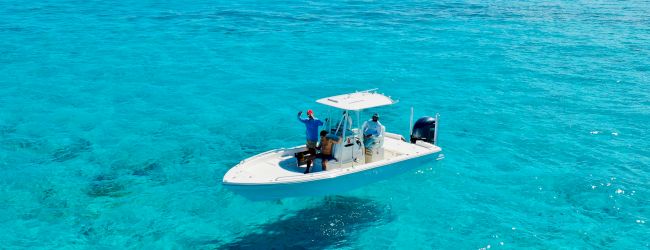 A small boat floating on clear turquoise sea, casting a shadow, with a bright blue sky above.
