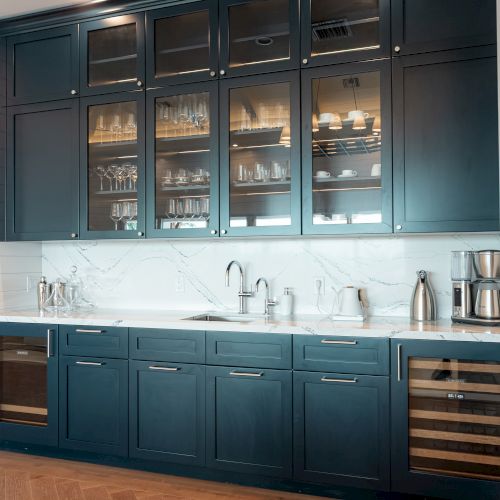 A dark, stylish bar with blue cabinetry, glass-fronted shelves, and warm lighting; polished wood floor and a neat, modern beverage setup.