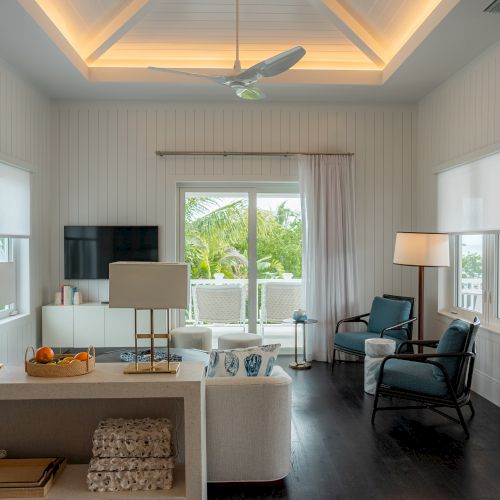 A bright, airy living room with a contemporary farmhouse vibe: neutral tones, blue-grey walls, white trim, a central chandelier, and natural light from large windows.
