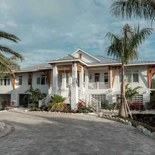 A stylish single-story house with a modern stucco facade, tropical palm trees, and a paved driveway, sunlit and inviting.