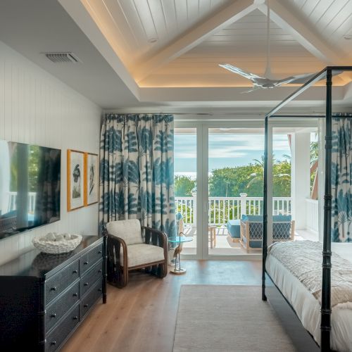 A bright, modern kitchen with a long island, sleek cabinets, pendant lights, and large windows overlooking a greenery-filled outdoor space.