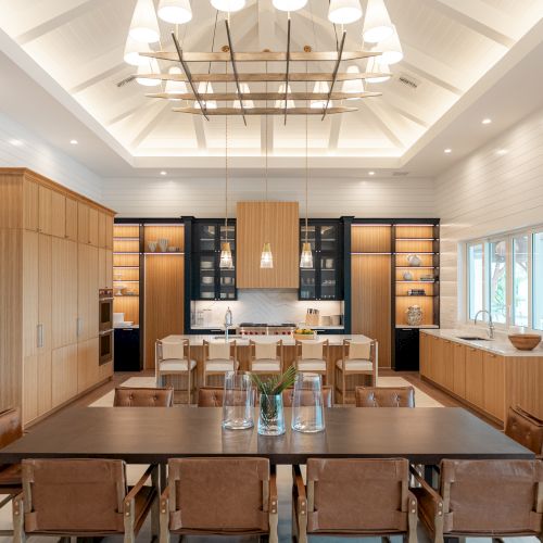 A bright, elegant dining room with a long wooden table, modern chairs, and a chandelier; warm wood tones, blue accents, and framed artwork along the walls.