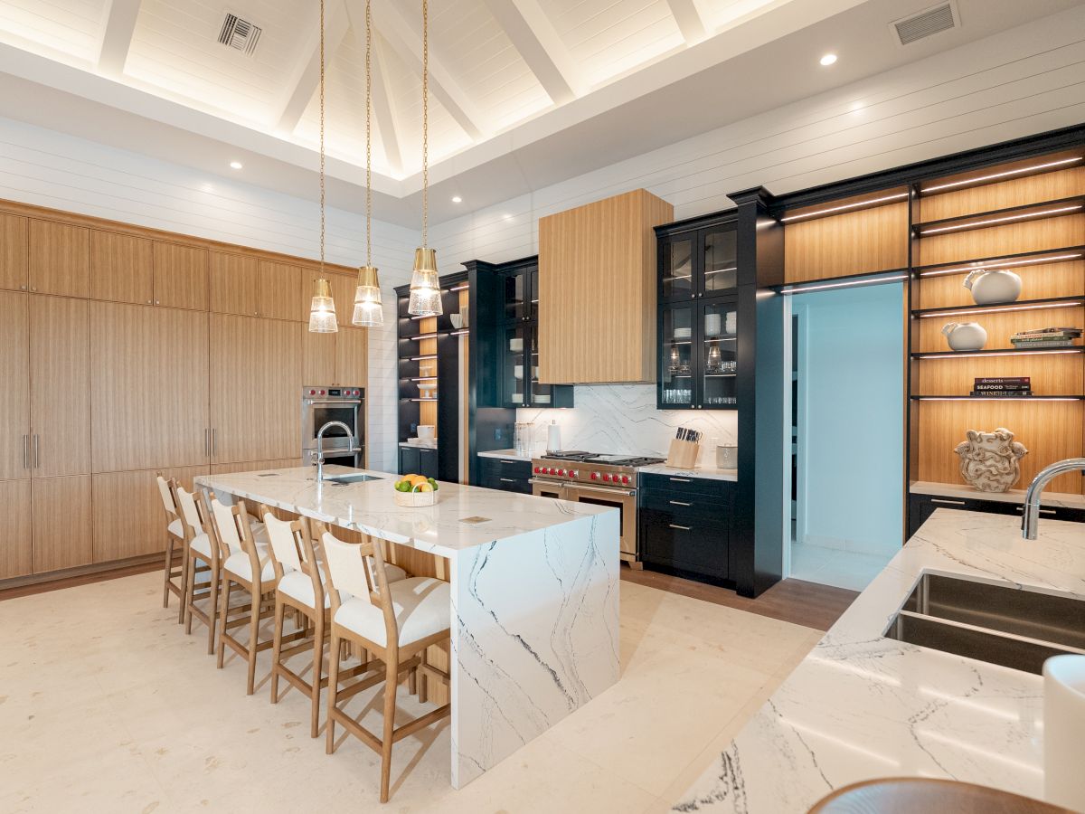 A modern, airy kitchen with a long white marble island, wooden dining table and chairs, black and wood cabinetry, open shelving, and a bright turquoise fridge. End sentence.