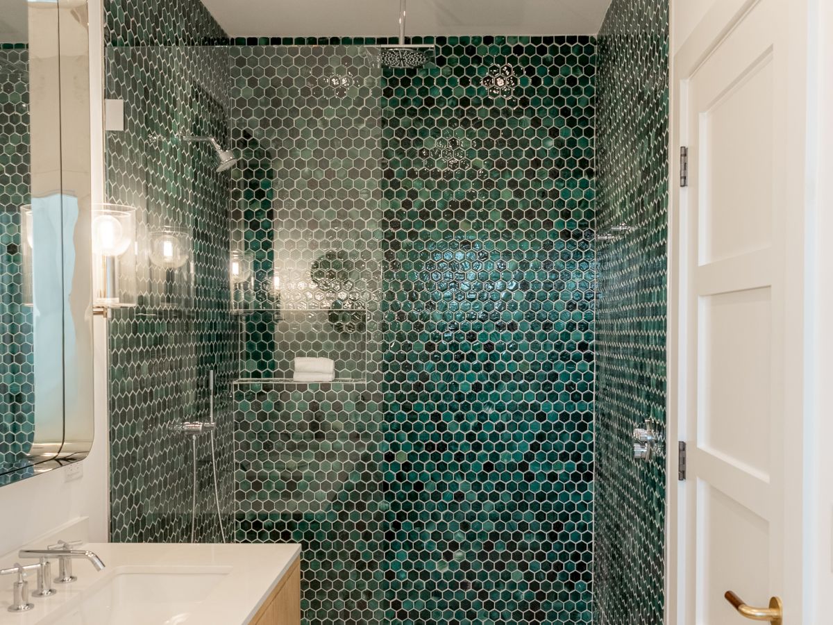 Bathroom with a glass-enclosed shower featuring dark green/teal hex tile walls, a white vanity, large mirror, and soft recessed lighting, clean and modern.
