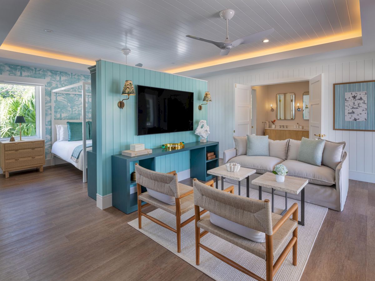 Bright living area with a teal partition, wall TV, and cozy seating; open doorway to a bedroom, light wood floors, coastal decor.