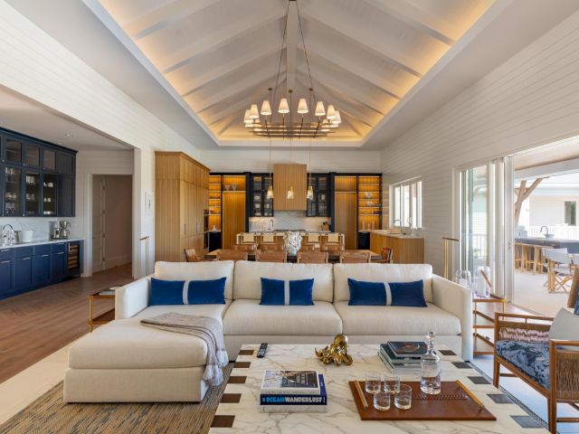 Bright modern kitchen and dining area with a long island, blue accents, pendant lights, and a white sofa in the foreground.