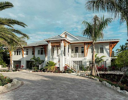 A sunny tropical house with a curved driveway, palm trees, and lush landscaping; a white, single-story home with a front porch.