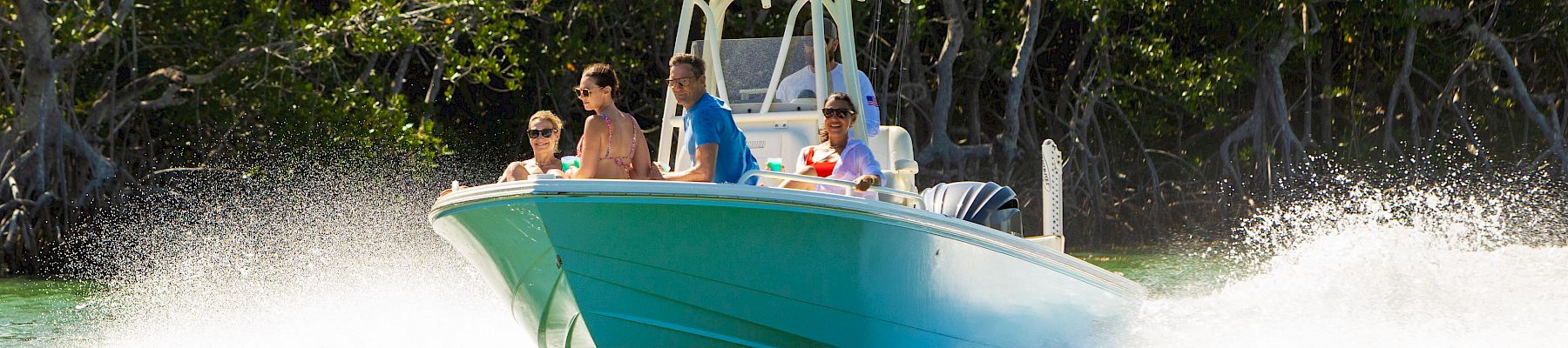 A group of people ride a green speedboat, grinning as it blasts through the water with a splash behind it.
